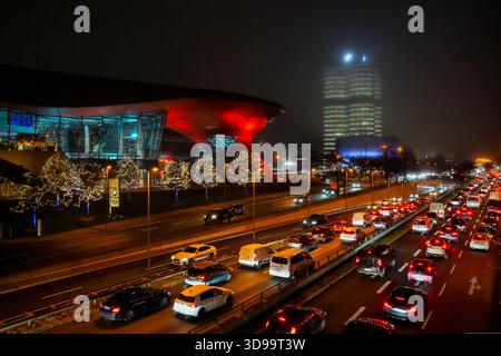 Vue sur l'anneau animé Mittlerer jusqu'au BMW Welt et au quatre cylindres BMW à Munich, illuminés de façon festive la nuit pendant la saison de l'Avent. Les deux Bui Banque D'Images