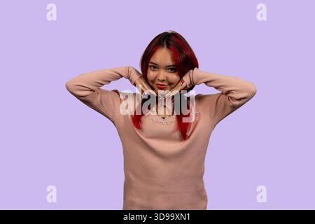 Photo studio d'une jeune femme aux cheveux roux encadrant son visage avec des mains et souriant sur un fond violet Banque D'Images