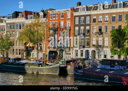 Maisons ensoleillées de Canalside avec barges le long d'une scène historique de front de mer d'Amsterdam Banque D'Images