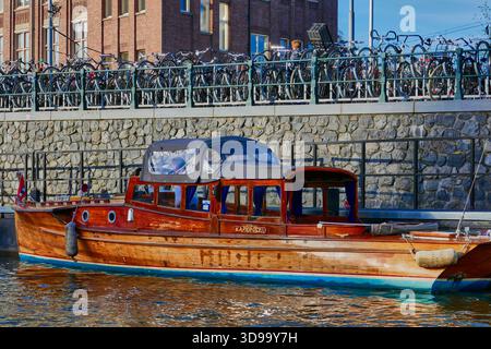 Bateau cabine en bois amarré dans le canal à côté du pont de parking à vélos dans la scène de front de mer urbaine à Amsterdam, Hollande Banque D'Images