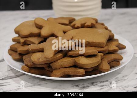 Une pile de biscuits en pain d'épices est placée sur une assiette blanche ronde. Les biscuits ont différentes formes telles que les étoiles et les gens en pain d'épices. Ils sont waitin Banque D'Images