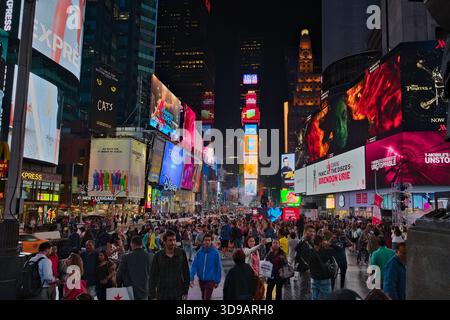 Times Square à New York la nuit est animé avec des foules de gens et des panneaux d'affichage lumineux colorés bordant les bâtiments. Banque D'Images