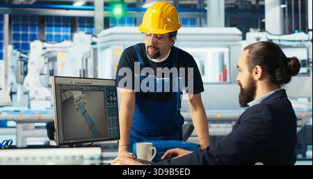 Gestionnaire d'usine photovoltaïque montrant à l'ingénieur sur l'écran du PC comment ajuster les paramètres du système. Spécialiste montrant membre du personnel comment optimiser l'approvisionnement en énergie dans l'usine de fabrication de panneaux solaires, caméra B. Banque D'Images