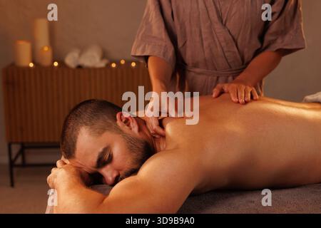 Un homme recevant un massage relaxant dans un environnement spa serein. Les mains du thérapeute travaillent doucement sur son dos, favorisant la relaxation et le bien-être Banque D'Images