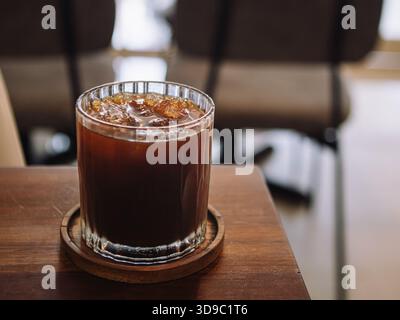 Espresso froid fraîchement infusé dans une tasse en verre moderne sur le dessus de la table en bois avec un environnement de café flou Banque D'Images