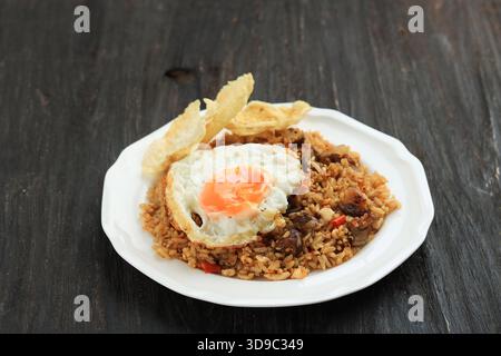 Riz frit de chèvre ou Nasi Goreng Kambing, servi avec œuf Sunny Side et craquelins, sur une assiette blanche Banque D'Images