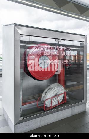 KL, Malaisie - Nov 27,2025 : enrouleur de tuyau d'incendie rouge stocké dans une armoire en verre transparent montée sur un mur, prêt pour une utilisation d'urgence dans un espace public. Banque D'Images