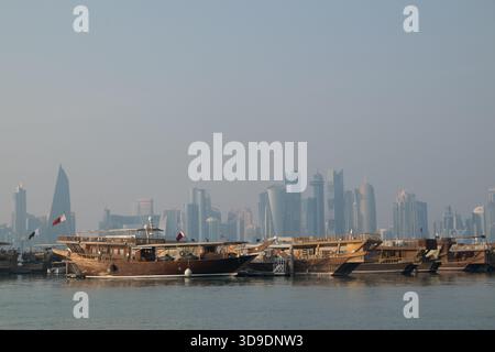 Des boutres en bois sont ancrés sur le front de mer de Doha, mettant en valeur le mélange de tradition et d'architecture moderne dans un ciel dégagé. Banque D'Images