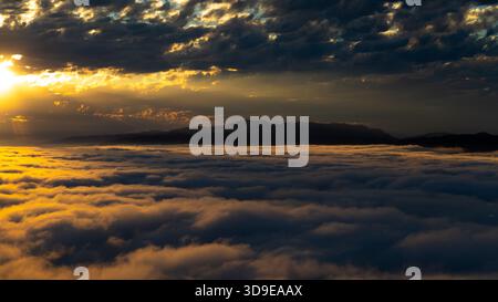 Vue aérienne d'un coucher de soleil doré sur une mer de nuages, avec des montagnes silhouettées au loin, Santa Monica, Californie, États-Unis. Banque D'Images