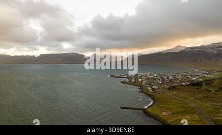 Vue aérienne de la ville nichée entre la mer sombre et les montagnes poussiéreuses de neige sous un ciel enflammé avec des teintes de coucher de soleil, Grundarfjardarbaer, Grundarfjarda Banque D'Images