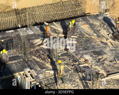 Vue des ouvriers de la construction en gilets jaune vif et casques de sécurité naviguent sur un chantier de construction occupé avec des barres d'armature et des planches en bois, Istanbul, Istanbul, Istanbul, Banque D'Images