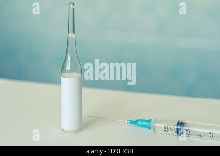Étiquette vierge flacon médical en verre et seringue en plastique pour injection sur fond bleu clair. Concept de vaccination, hormone insulinique et injection cosmétique Banque D'Images