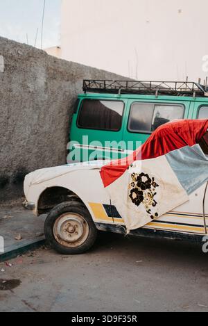 Vieille voiture recouverte de tissu coloré à côté de Van à Aourir, Maroc Banque D'Images