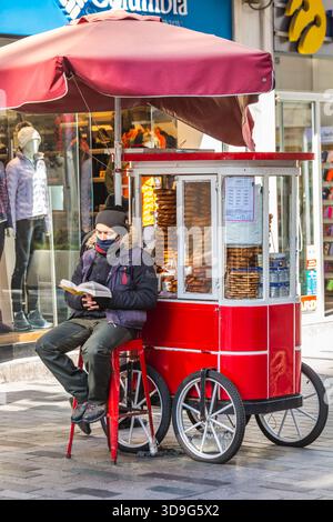 Homme lisant un livre tout en vendant un bagel de fast food turc appelé simit. Rue principale à Istanbul en Turquie. Istanbul, Turquie - 10 février 2022. Banque D'Images