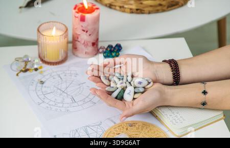 Mains tenant un ensemble de pierres de rune, avec des cartes astrologiques en arrière-plan. Dire la fortune. Banque D'Images