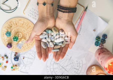 Mains tenant un ensemble de pierres de rune, avec des cartes astrologiques en arrière-plan. Dire la fortune. Banque D'Images