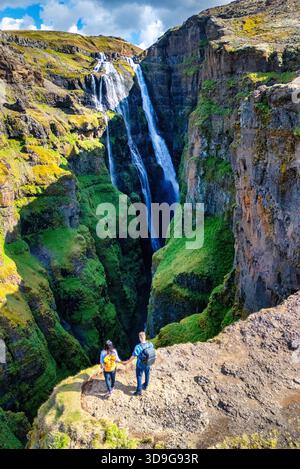 Deux randonneurs aventureux se tiennent au bord d'une falaise rocheuse, contemplant une cascade à couper le souffle qui tombe en cascade dans une gorge profonde. Glymur Waterfall Iceland || autorisation du modèle Banque D'Images
