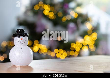 Décoration de bonhomme de neige en verre sur une table en chêne avec des lumières bokeh festives chaudes en arrière-plan, scène de vacances saisonnière joyeuse Banque D'Images