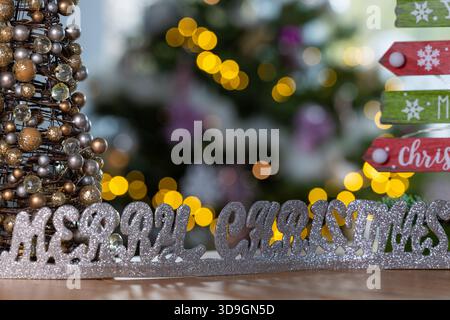 Décoration de joyeux Noël à côté d'un signe coloré de joyeux Noël avec des lumières bokeh festives chaudes en arrière-plan, scène de vacances saisonnière joyeuse Banque D'Images