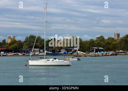 Orford Quay, Suffolk, Angleterre, Royaume-Uni - Yachts et bateaux amarrés au quai. Au loin se trouvent les tours du château d'Orford et l'église Saint-Barthélemy Banque D'Images