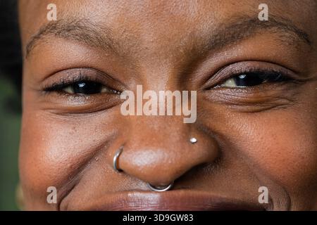 Femme adulte afro-américaine montrant la peau et des piercings de nez argentés contre un mur vert flou Banque D'Images