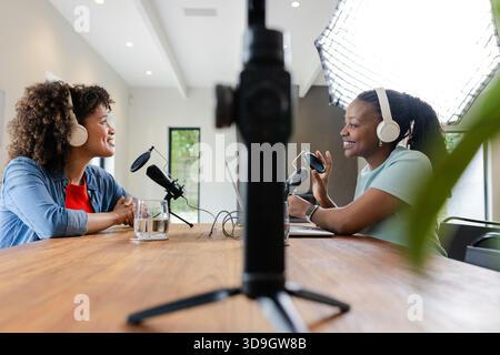 Diverses amies enregistrant un podcast dans une salle de studio à l'aide de deux microphones, caméra, écouteurs Banque D'Images
