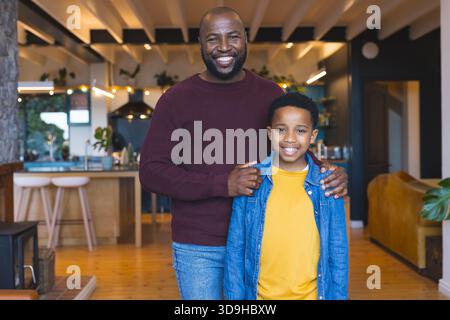 Père afro-américain et fils partageant des sourires dans la cuisine de la maison avec îlot en bois et plantes en pot Banque D'Images