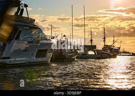 Un yacht club au coucher du soleil, des yachts et des voiliers sont amarrés aux couchettes, d'énormes défenses accrochées à des méga yachts, des cordes épaisses, des reflets sur les côtés brillants Banque D'Images