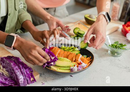 Couple diversifié assemblant bol poke noir avec avocat sur comptoir en marbre dans la cuisine à la maison Banque D'Images
