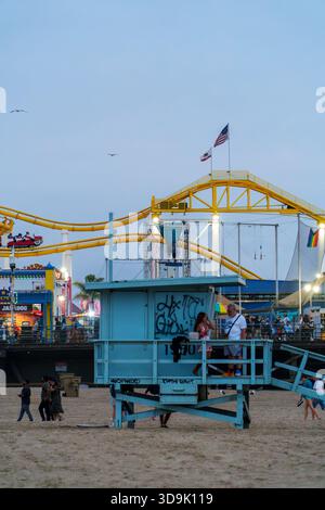 Santa Monica, CALIFORNIE, États-Unis. 26 septembre 2025. - Les gens se promènent sur la plage et la jetée comme les manèges du parc d'attractions illuminent contre le ciel crépusculaire, centré Banque D'Images