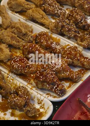 Ailes de poulet frites coréennes appétissantes avec sauce sucrée et épicée et graines de sésame. Délicieux et croustillant snack asiatique de Street food affiché sur pla blanc Banque D'Images