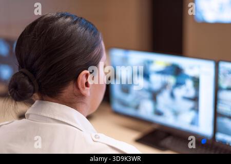 Opérateur de sécurité féminin observant de près plusieurs flux de vidéosurveillance à l'intérieur d'une salle de contrôle high-tech. Banque D'Images