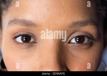 Femme afro-américaine adulte présentant les yeux bruns et le nez dans un espace légèrement éclairé avec boucle d'oreille cerceau Banque D'Images