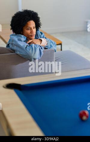 Homme afro-américain appuyé sur un canapé dans le salon de jeux, regardant la table de billard en feutre bleu, espace photocopie Banque D'Images