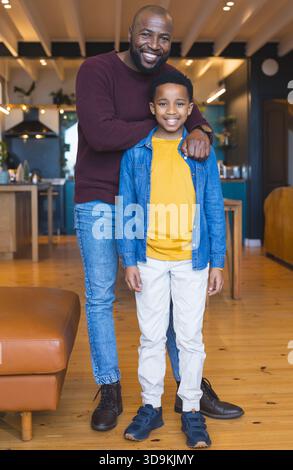 Père afro-américain et fils debout et souriant dans la cuisine ouverte près du pouf en cuir Banque D'Images