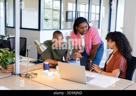 Collègues afro-américains collaborant autour du bureau en bois dans le bureau moderne en utilisant un ordinateur portable et des papiers Banque D'Images