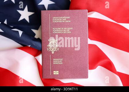 Passeport belge sur grand drapeau agitant des États-Unis d'Amérique close up. Visa AMÉRICAIN et concept d'immigration Banque D'Images