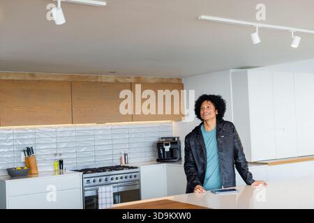 Homme afro-américain penché sur l'île visionnant la tablette par machine à expresso dans la cuisine, espace de copie Banque D'Images
