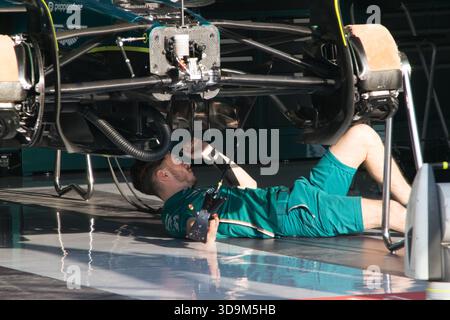 Un travailleur est allongé sur le sol pour effectuer des travaux d'entretien sous une voiture de course dans la zone des stands pendant le Grand Prix de formule 1 du Qatar 2025. Banque D'Images