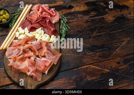 Plateau de charcuterie gastronomique composé de salumi italien, de cubes de fromage, d'olives et de gressins disposés sur un fond en bois Banque D'Images