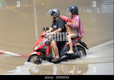 BANGKOK, THAÏLANDE, nov 09 2025, couple conduit une moto avec une charge à travers l'eau dans une rue inondée Banque D'Images