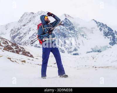 Randonneur de montagne avec des bâtons de trekking regardant au loin sur une crête alpine enneigée pendant l'expédition d'hiver Banque D'Images