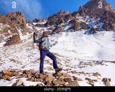 Touriste de montagne avec des bâtons de trekking se dresse sur les pierres d'une crête alpine enneigée lors d'une expédition hivernale Banque D'Images