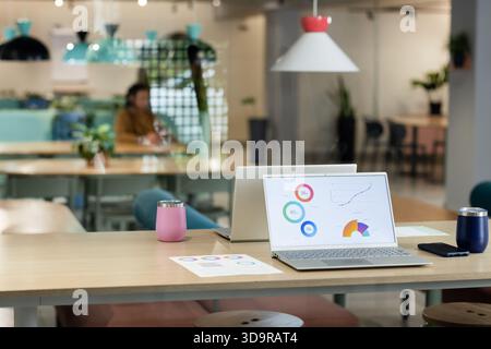 L'ordinateur portable en argent ouvert affiche des tableaux et des graphiques sur une table en bois avec des gobelets roses et marins Banque D'Images