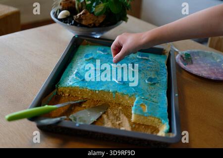 La main d'un enfant atteint pour une figurine de gomme à vin sur un gâteau de feuille bleue à une fête d'anniversaire d'enfants avec le thème du monde sous-marin Banque D'Images