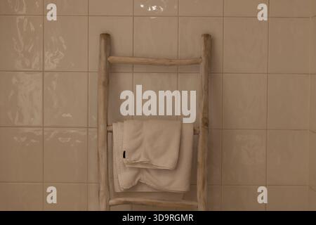 Un porte-serviettes en bois échelle contre un mur de salle de bain carrelé avec une serviette blanche pliée. Banque D'Images
