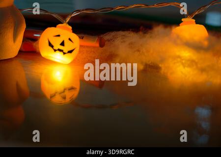 Une petite guirlande de citrouille souriante se trouve sur la table dans le cadre du décor d'Halloween. Un coton blanc doux lui confère une touche effrayante et festive. Banque D'Images
