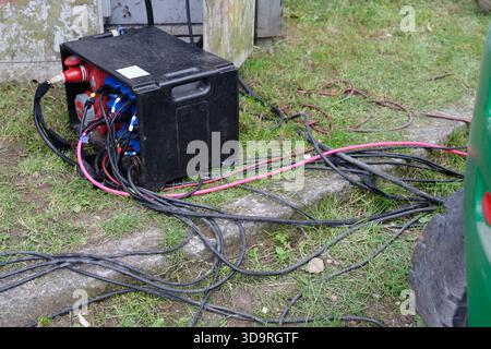 Un boîtier de distribution électrique portable noir avec plusieurs câbles industriels et connecteurs se trouve sur une zone herbeuse, fournissant de l'électricité pour les équipements d'extérieur Banque D'Images