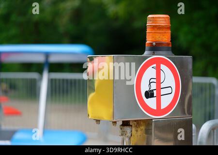 Un poteau métallique avec un voyant d'avertissement jaune sur le dessus affiche un autocollant « interdiction de fumer » avec un symbole de cigarette barrée. Le poteau se tient à l'extérieur, signalant Banque D'Images