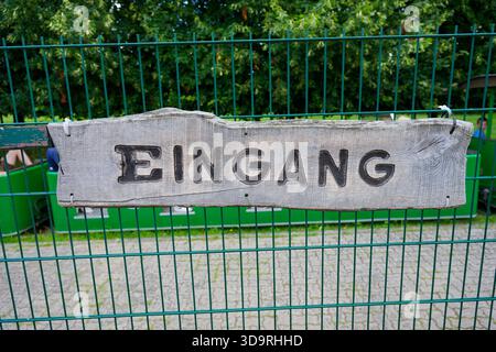 Une petite clôture métallique faite de tiges verticales tient une planche de bois avec le mot Eingang écrit dessus tandis qu'un train de jouets vert est visible dans le dos Banque D'Images